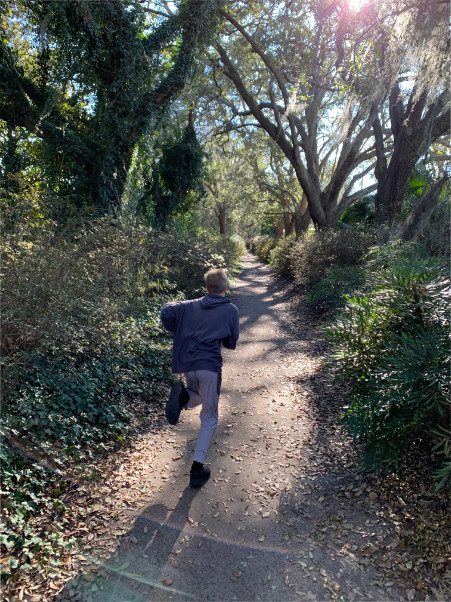 Boy running down dirt path with dark vegetation on either side
