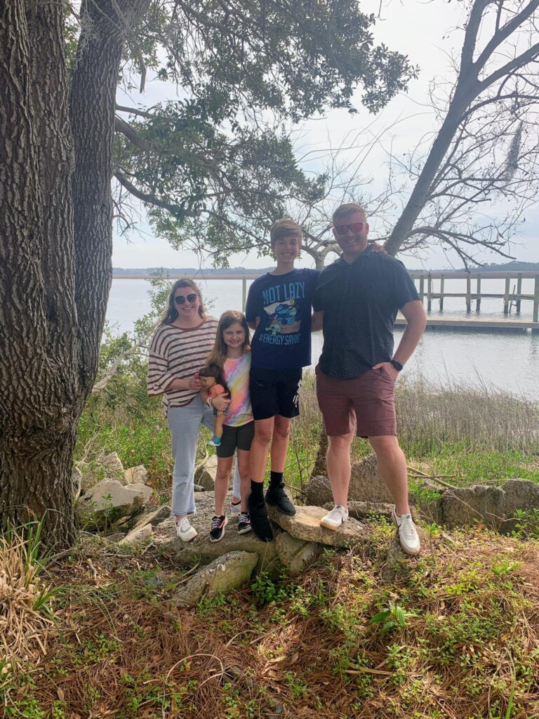 Couple and two kids smiling for pictures with water behind