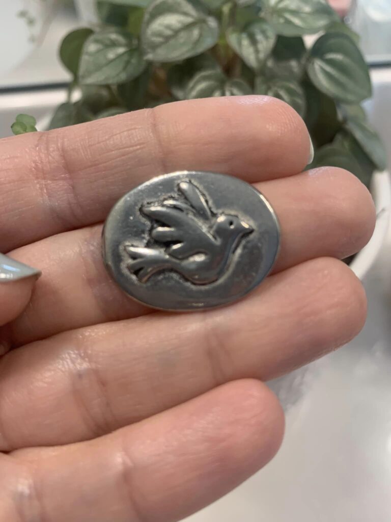 small silver and round trinket with dove on it